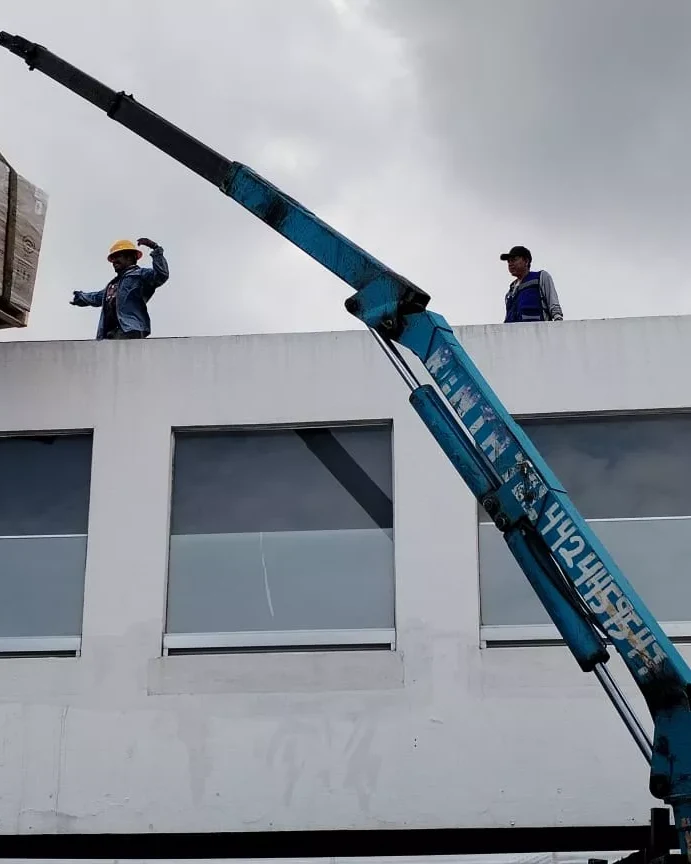 Técnicos maniobrando una grúa para subir material a la azotea de un edificio comercial